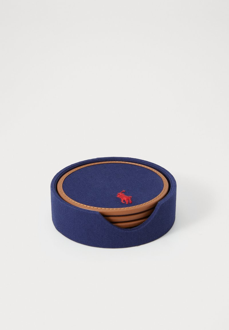 Runde coasters i marineblått stoff med herringbone-mønster, med en brun lærkant og en rød brodert logo i midten.