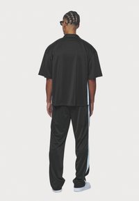Black matching sports set featuring a loose-fitting short-sleeve top and relaxed pants with an accent stripe. Made of smooth, lightweight fabric.