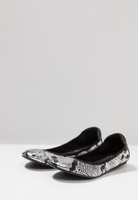Scarpe basse nere e argento con un motivo texturizzato a forma di serpente, posizionate su uno sfondo grigio chiaro. Hanno la punta arrotondata e bordi morbidi.