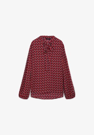 Blusa rossa con un motivo geometrico di piccoli triangoli in bianco e grigio. Presenta maniche lunghe e un fiocco al colletto. Tessuto leggero.