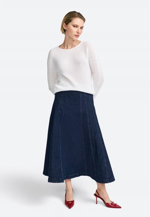 Pullover di lana bianca, gonna a trapezio in denim scuro con cuciture in evidenza e décolleté rossi a punta. Tessuto liscio, design casual.