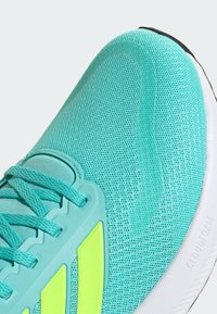 Turquoise athletic shoe with mesh upper, textured accents, bright yellow details, and a cushioned white sole marked "CLOUDFOAM."