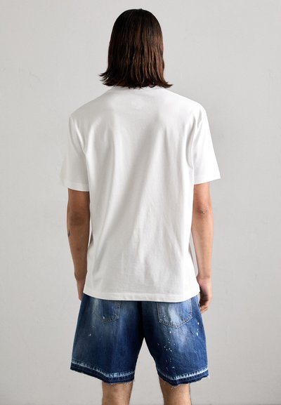 T-shirt bianco in cotone con maniche corte, caratterizzato da una vestibilità comoda. Abbinato a pantaloni shorts in denim scuro con orlo sfrangiato e tasche.