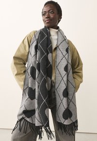 Gray scarf featuring a diamond pattern with black hearts, finished with fringe edges. Made from a soft textile material.