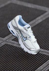 White athletic shoe with mesh and synthetic material, light blue accents, and a black swoosh logo. Features laces and textured sole.