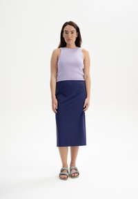 Paarse geribbelde tanktop gecombineerd met een marineblauwe rok. De rok heeft een elastische tailleband. De schoeisel bestaat uit grijze sandalen met een gesp.