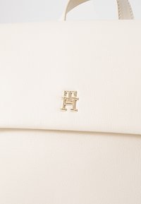 Crème faux leren handtas met een gestructureerd ontwerp, een gestructureerde vorm en een goudkleurig logo accent aan de voorkant.