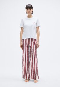 T-shirt blanc avec un petit motif rouge et un pantalon large à rayures rouges et blanches. La tenue est décontractée et en tissu léger.