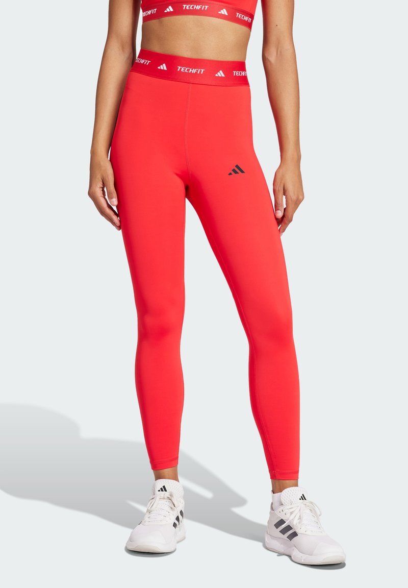 Czerwone legginsy kompresyjne o gładkiej teksturze, z wysokim stanem i logo "TECHFIT" oraz małym czarnym znakiem na udzie.