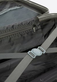 Interno di una valigia grigia con tasca a rete con zip, cinghie regolabili e fodera con marchio. Texture liscia con motivi sottili.