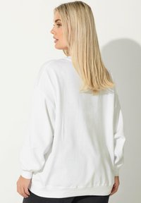 Vit oversized sweatshirt med lång ärm, ribbade muddar och nederkant, mjuk textur och minimalistisk design. Inga synliga logotyper eller mönster.