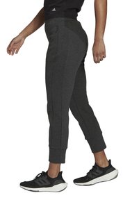Dunkelgraue Sporthosen mit schmal zulaufendem Schnitt, Bündchen an den Knöcheln, Seitentaschen und einer glatten Textur, kombiniert mit schwarzen Sportschuhen.