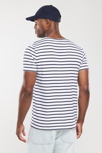 Gestreept T-shirt met korte mouwen in wit en marineblauw, met een ronde halslijn. Gedragen met lichtgekleurde spijkerbroek en een navy pet.