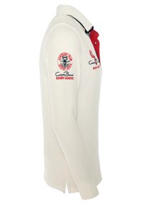 Hvid langærmet polo skjorte med rød krave, prydet med broderede logoer i rød og sort på brystet og ærmerne. Sideslidser i nederkanten.