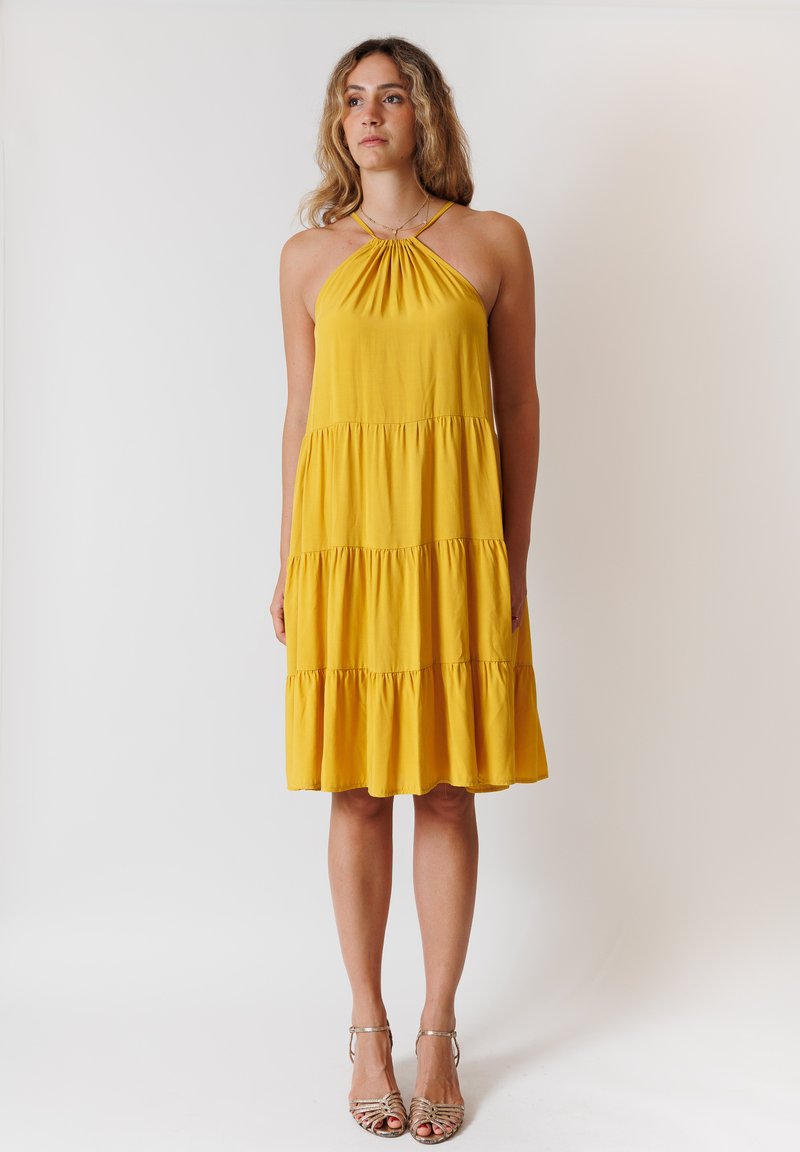 Abito giallo senza maniche con scollatura a halter, caratterizzato da un colletto arricciato e una gonna a strati. Realizzato in un tessuto morbido con una silhouette fluida.