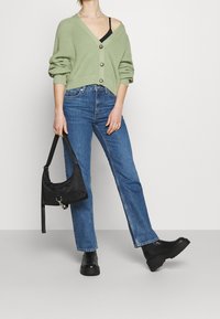 Ljusgrön ribbade kofta med tre knappar, bärs över en svart linne. Blå högmidjade jeans och svarta platåstövlar. Svart axelväska.