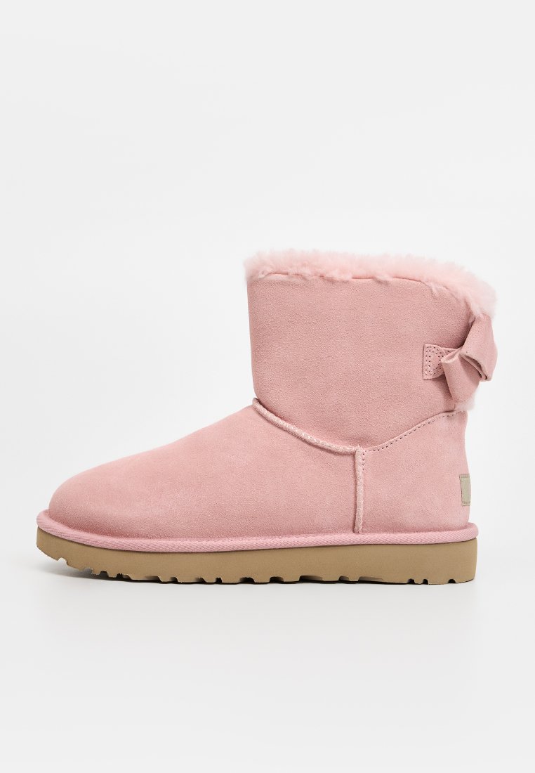 Rosa Wildleder-Stiefelette mit einem weichen Kunstfellfutter, runder Zehenpartie, flacher Gummisohle und einer dekorativen Schleife an der Seite.