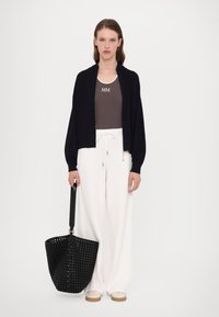 Svart strikket cardigan, mørkebrunt tanktop med "MM"-logo, hvite vide bukser, svart vevd totebag og lyse sko.