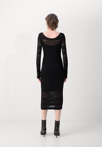 Abito nero lavorato a maglia con maniche lunghe, lunghezza a metà polpaccio, con un design a motivi e un collo rotondo. Abbinato a stivali neri alla caviglia.