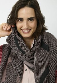Grande écharpe à motifs en rose et noir, présentant un tissage texturé. L'écharpe est drapée librement autour du cou. Une chemise à boutons est en dessous.