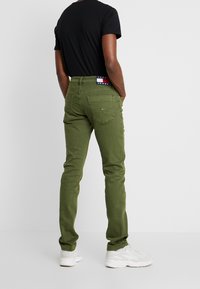 Gröna slim-fit byxor i bomull, med femficksdesign, bakre logopatch och ankellång fåll, kombinerade med en svart t-shirt.