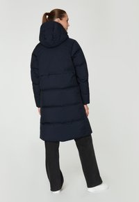 Abrigo puffer azul marino con capucha, con un diseño acolchado y un corte de longitud media. Llevado con jeans negros y zapatillas blancas.