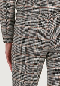 Geklede broek in zwart, wit en bruin met een houndstooth- en geometrisch patroon. De stof lijkt een structuur te hebben met een getailleerde pasvorm.