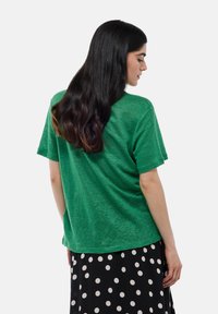 T-shirt vert à manches courtes en tissu doux et texturé, associé à une jupe noire à pois. Le t-shirt a une coupe décontractée et un col rond.