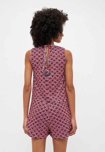 Bežėklių romperis turi geometrinį raštą raudonos, baltos ir mėlynos spalvų. Jis turi iškirptę nugaroje su ryšuliu, tekstūruotą audinį ir šortus.