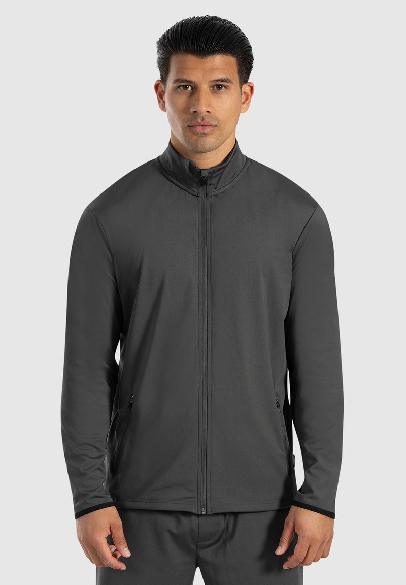 Chaqueta deportiva gris con cuello alto, cierre de cremallera completo, dos bolsillos laterales y mangas largas, fabricada con un material suave y ligero.