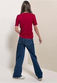Red short-sleeve top paired with high-waisted, wide-leg blue denim jeans. The outfit is completed with white sneakers and casual fit.
