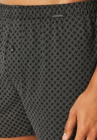 Black patterned boxers with an elastic waistband, featuring a small button and a subtle, woven texture. Brand label visible at the waistband.