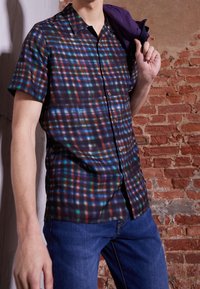 Camicia a maniche corte con bottoni in tessuto scuro con un motivo a quadri multicolore. I singoli quadrati presentano tonalità di blu, verde e rosso.