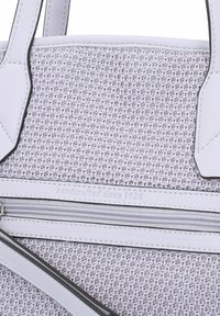 Handgemaakte totebag met een gestructureerd lavendelkleurig lichaam, witte leren accenten en een zilveren rits. Voorzien van de inscriptie "handgemaakt sinds 1928".