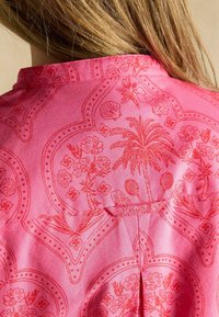 Rosa gemustertes Kleidungsstück mit floralem und muschelförmigem Design sowie feinen Details. Weicher Stoff mit glatter Textur und einem Rückenschlitz.