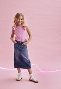Rosa ärmelloses Oberteil mit Spitzendetails, kombiniert mit einem langen Jeansrock. Ausgestattet mit weißen und beigen Sneakers, die eine strukturierte Oberfläche aufweisen.