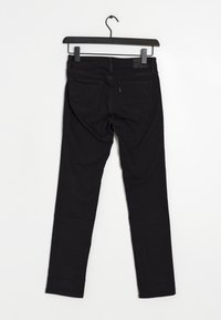 Jean noir slim-fit suspendu à un cintre noir à pince, vu de dos avec les poches arrière et les passants de ceinture visibles.
