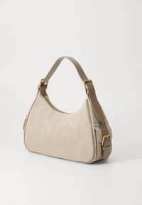 Μπεζ σουέτ τσάντα ώμου με λείο δερμάτινο λουρί, χρυσές αγκράφες, κλείσιμο με φερμουάρ και ανάγλυφο λογότυπο στο κέντρο μπροστά.