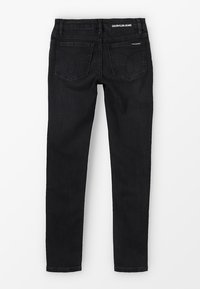 Jeans ajustados negros de denim. Presentan una cintura de altura media, dos bolsillos traseros con diseños de flechas y una etiqueta de Calvin Klein Jeans en el cinturón.