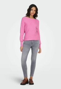 Lys rosa strikket genser med båthals og lange ermer, kombinert med grå skinny jeans og brune ankelstøvler med snøring.