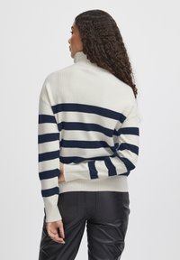 Pull en laine avec col haut, fond crème et rayures horizontales marines, présentant des poignets côtelés et une coupe décontractée. Vue de dos mise en avant.