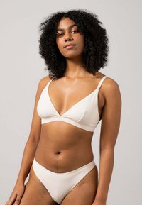 Witte naadloze bralette met een V-hals, verstelbare bandjes en bijpassende hipsteronderbroek. Stof heeft een zachte, licht gestructureerde afwerking.