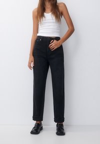 Černé džíny s vysokým pasem, volného střihu, s ohrnutými manžetami, pětikomorovým designem a zapínáním na knoflík. Kombinované s bílým tílkem.