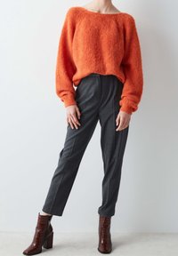 Suéter naranja de felpa con escote amplio, combinado con pantalones grises de corte ajustado. Botines marrones con relieve de cocodrilo y tacones gruesos.