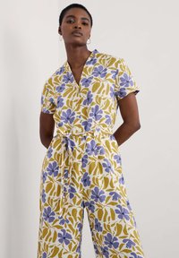 Blommig jumpsuit i gula och lila nyanser. Korta ärmar, V-krage, bälte i midjan och knappar fram. Mjuk tygkänsla.