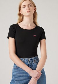 Black short-sleeve fitted t-shirt with a round neckline and a small red Levi's logo on the chest, paired with light blue high-waisted jeans.