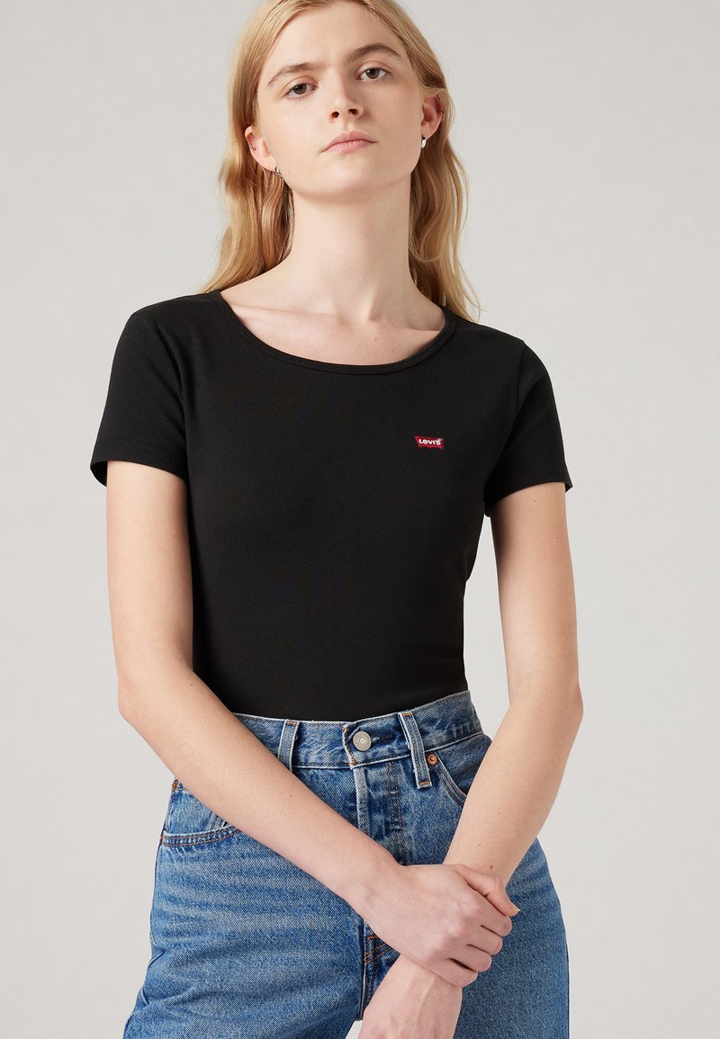 T-shirt noir à manches courtes et cintré avec un col rond et un petit logo rouge Levi's sur la poitrine, associé à un jean taille haute bleu clair.
