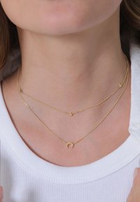 Goldene Halsketten übereinander geschichtet; eine hat einen kleinen Halbmond-Anhänger, die anderen haben winzige Sternakzente. Die glatte, feine Kettentextur fühlt sich angenehm auf der Haut an.