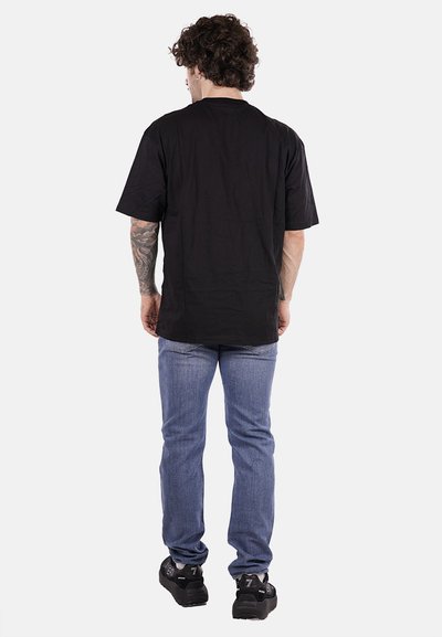 T-shirt nera a maniche corte, vestibilità comoda, in cotone. Abbinata a jeans in denim azzurro chiaro e sneakers nere, mostrano uno stile semplice e informale.