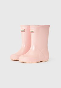 Bottes de pluie en caoutchouc rose avec une texture lisse, un bout arrondi et une hauteur de cheville basse. Présente deux étiquettes avec la marque "HUNTER".